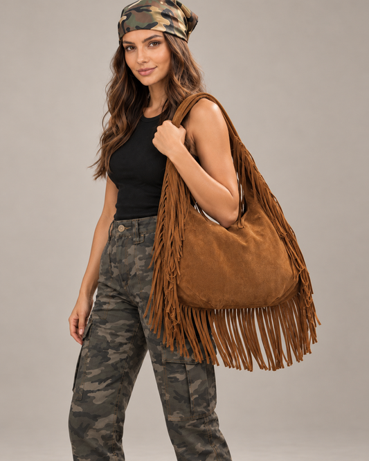 Bolso de hombro de piel con flecos en el asa y la base camel, llevado por una modelo.