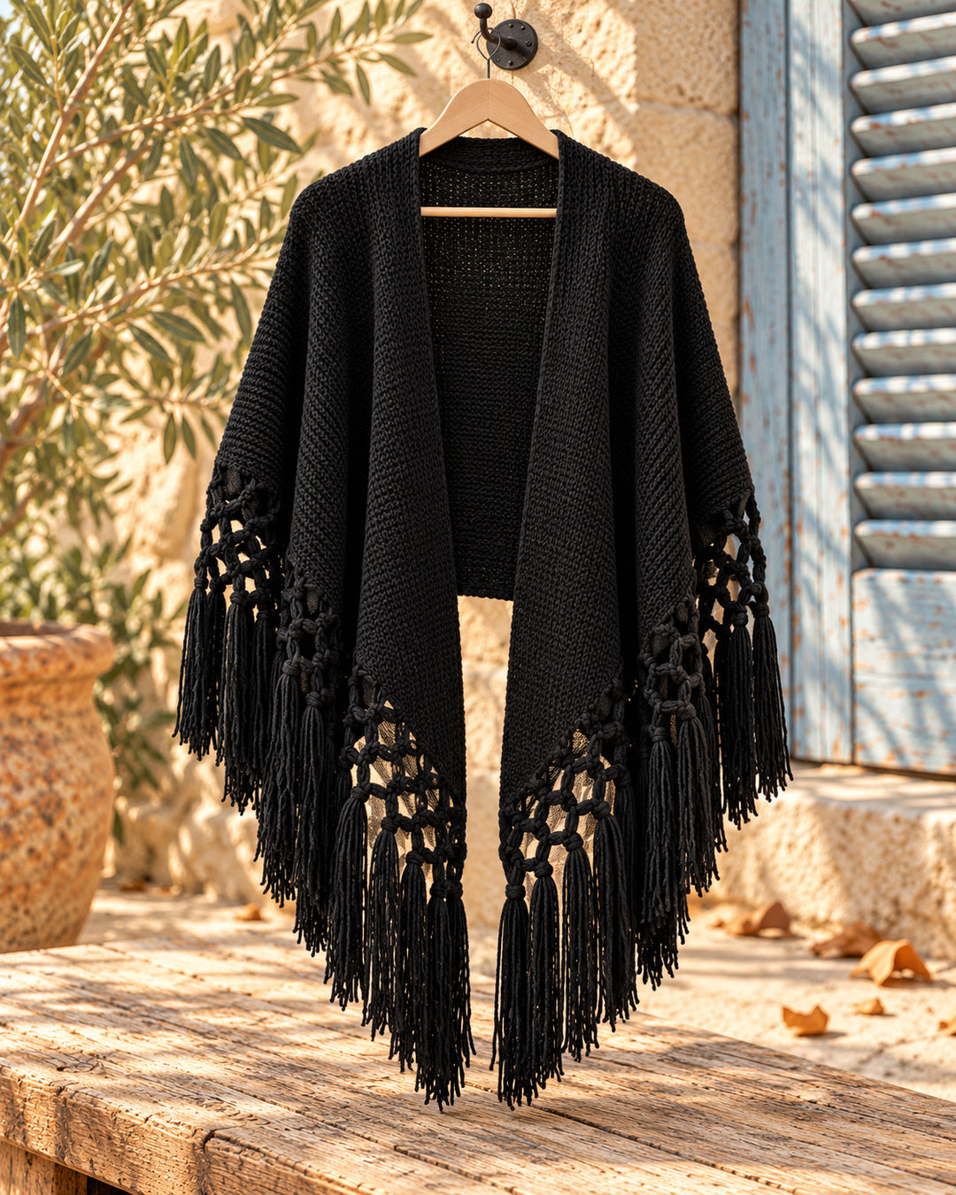 Chal poncho abierto de punto con nudos y flecos en color negro, vista del producto en percha.