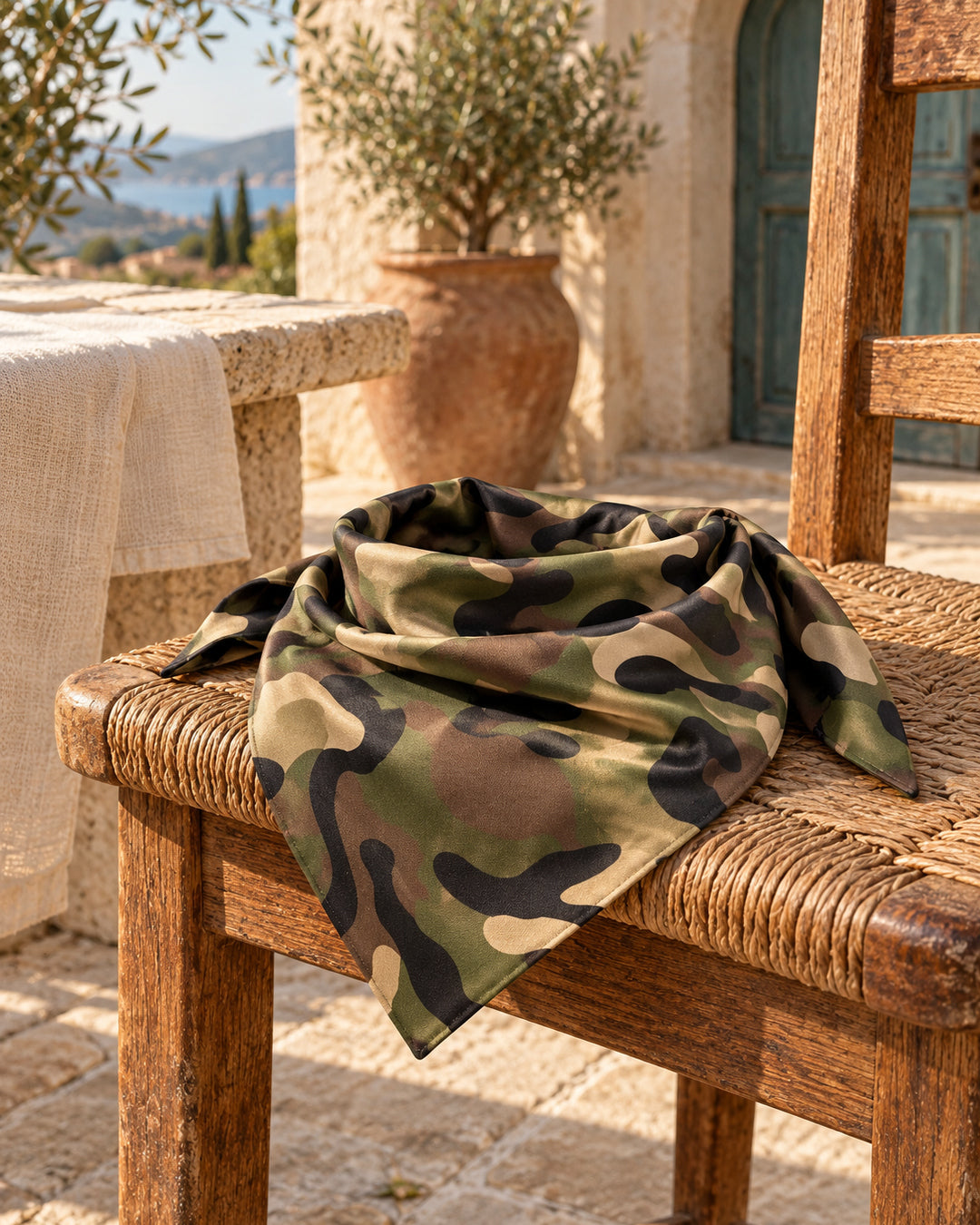 Bandana de camuflaje en tonos verdes, marrones y negros, colocada sobre una silla de madera.