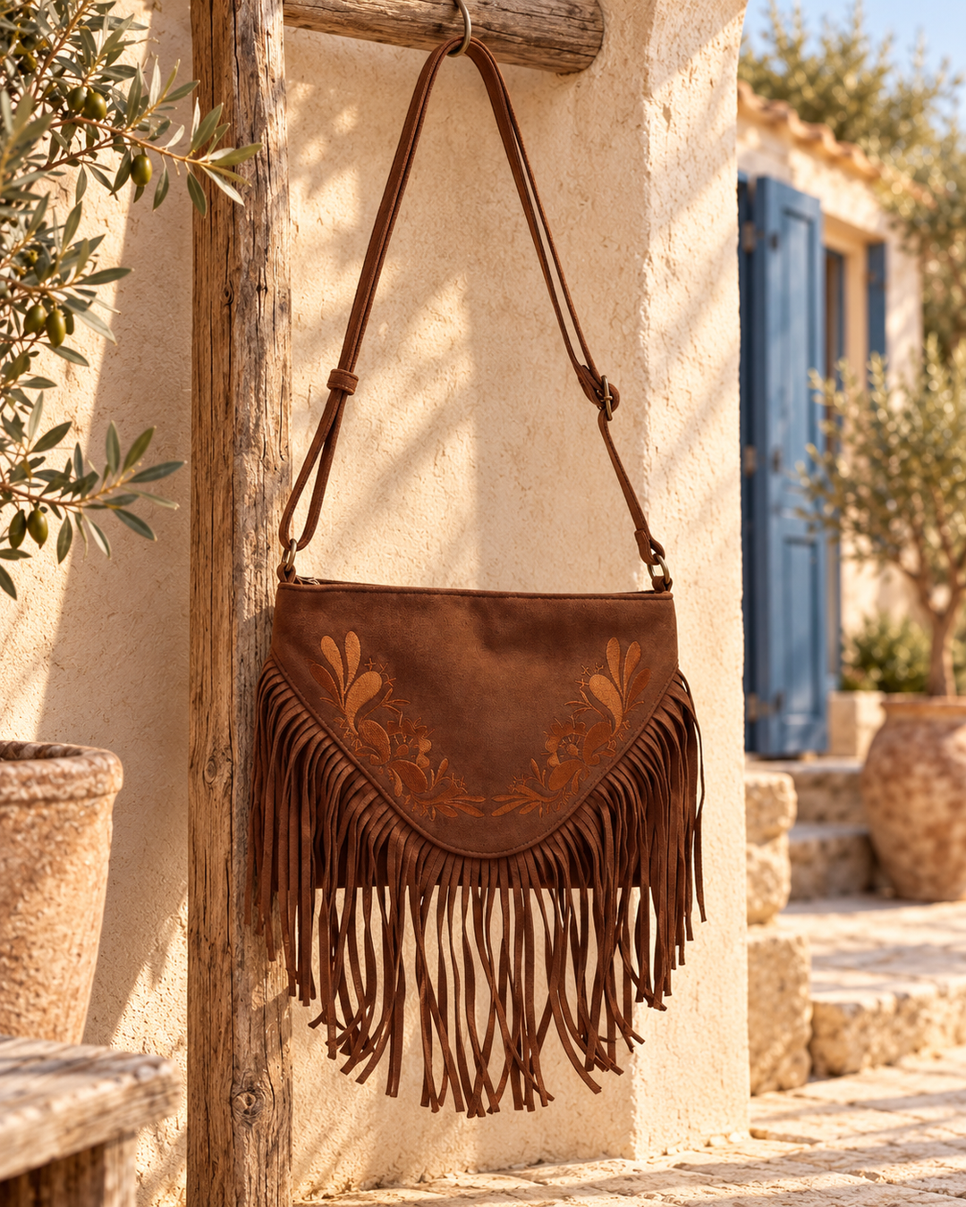 Bandolera de piel con flecos y bordado vegetal marrón, bodegón en un patio mediterráneo.