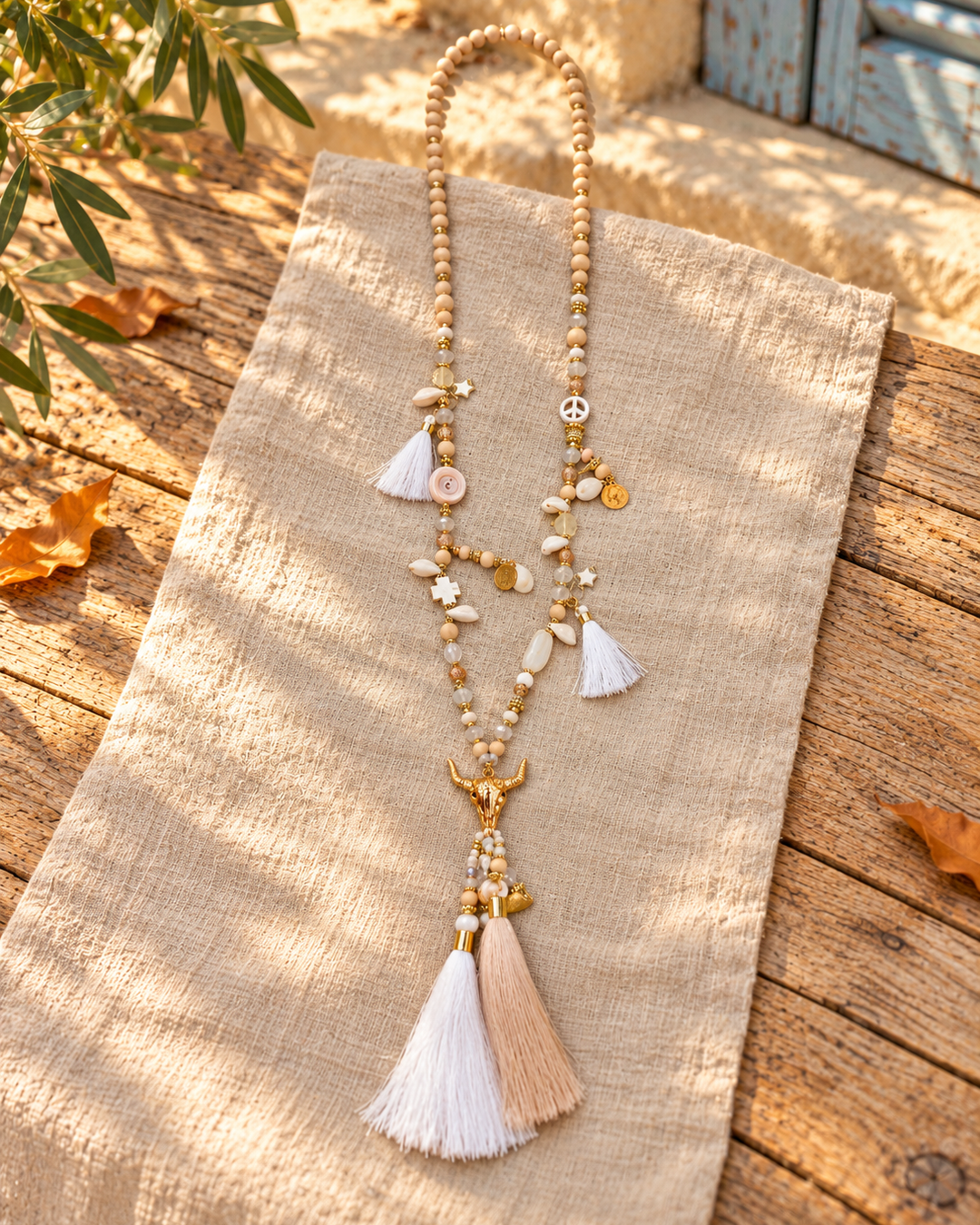 Collar largo boho calavera de toro · blanco y dorado, bodegón sobre tejido claro