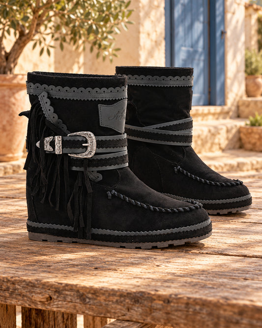 Botas boho de piel con remates festoneados · Mulanka, color negro, bodegón del par sobre madera en un patio mediterráneo.