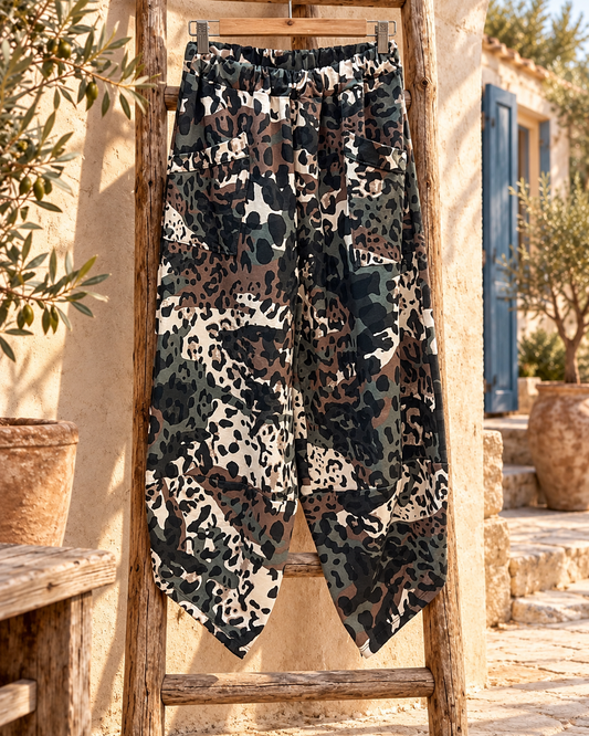 Bodegón del pantalón asimétrico de camuflaje, completo y en percha sobre una escalera de madera en un patio mediterráneo.