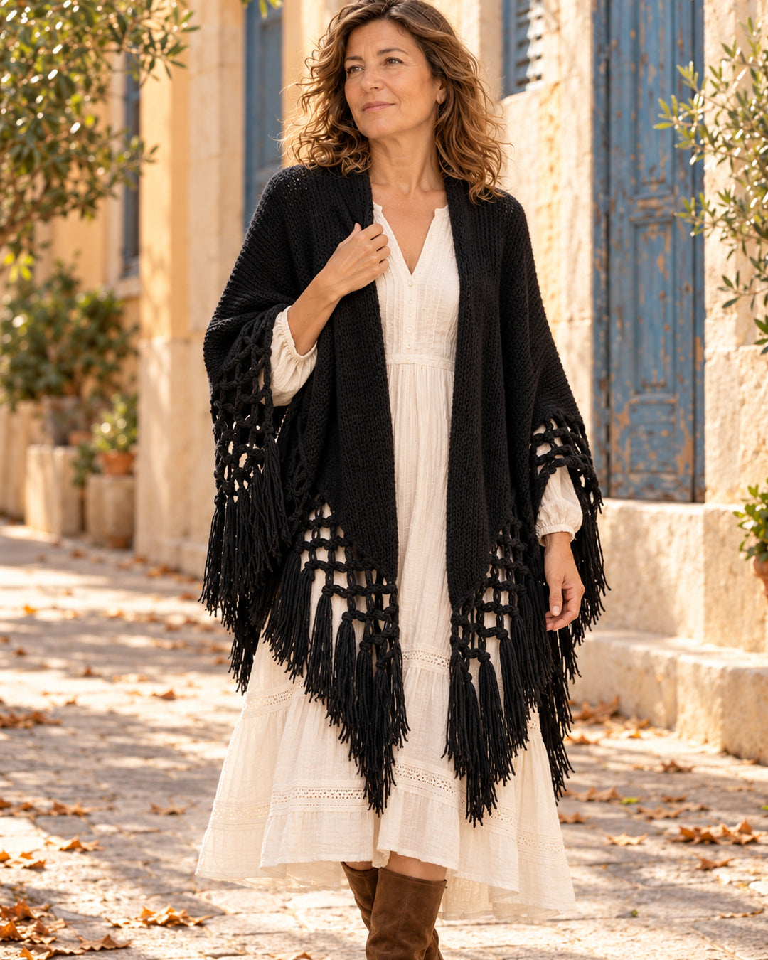 Chal poncho abierto de punto con nudos y flecos en color negro, llevado sobre vestido marfil.