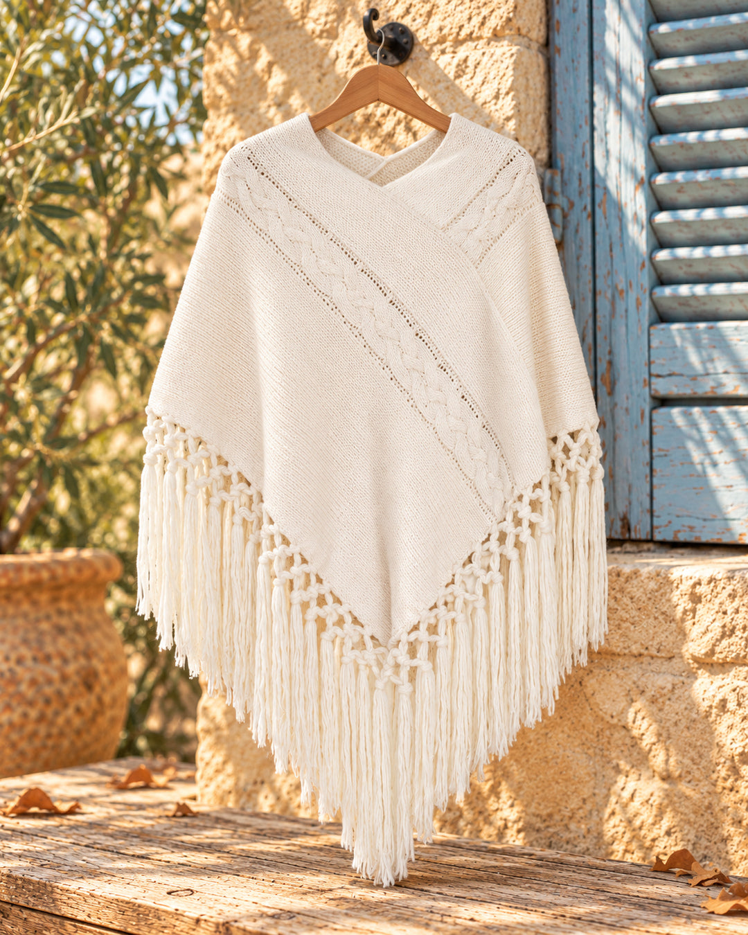 Poncho cerrado de punto con escote en V y flecos en color blanco, vista del producto en percha.