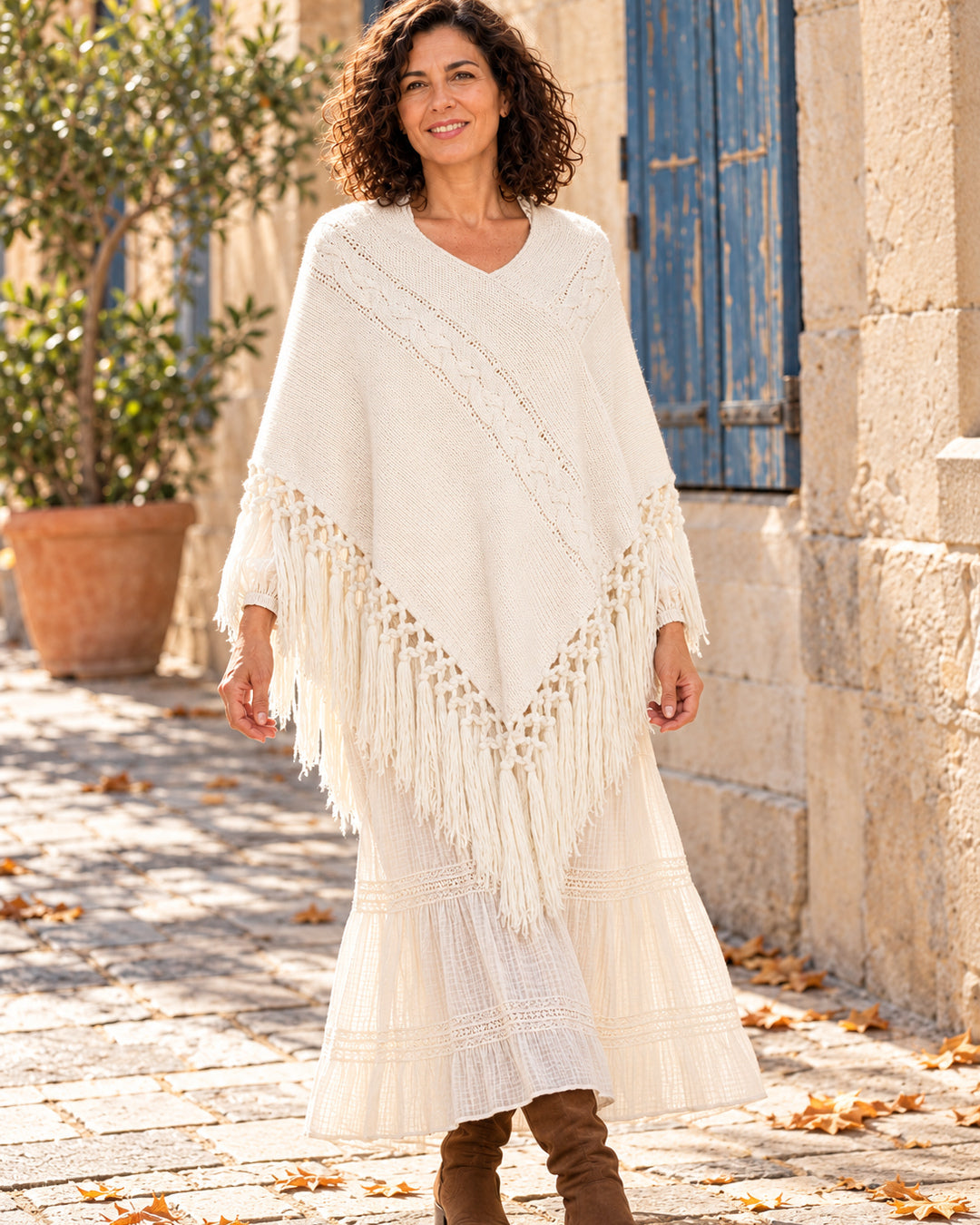 Poncho cerrado de punto con escote en V y flecos en color blanco, llevado sobre vestido marfil.