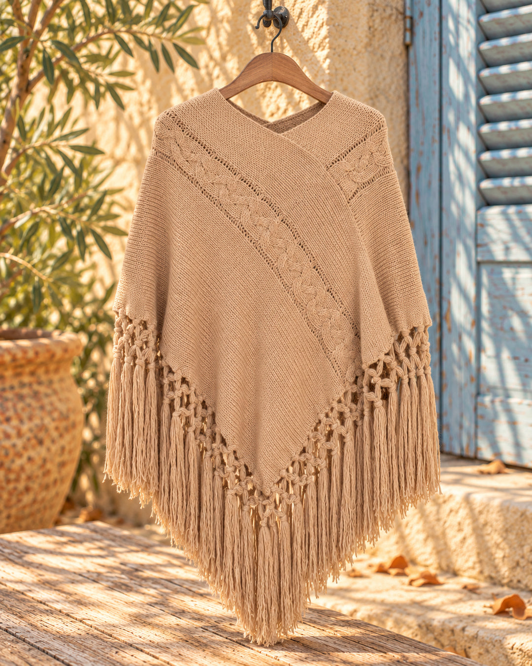 Poncho cerrado de punto con escote en V y flecos en color camel, vista del producto en percha.