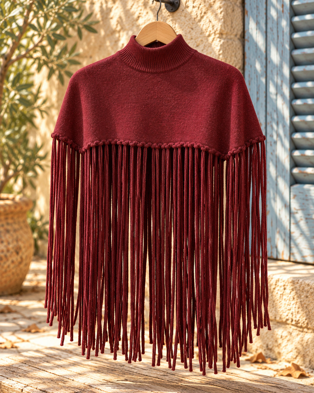 Poncho corto de cuello alto con flecos largos en color burdeos, vista del producto en percha.