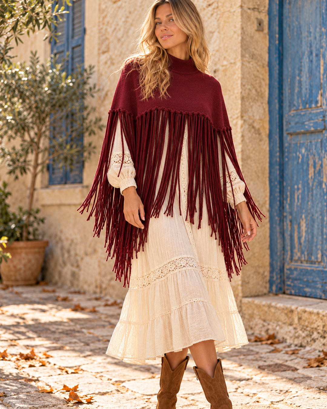 Poncho corto de cuello alto con flecos largos en color burdeos, llevado sobre vestido marfil.