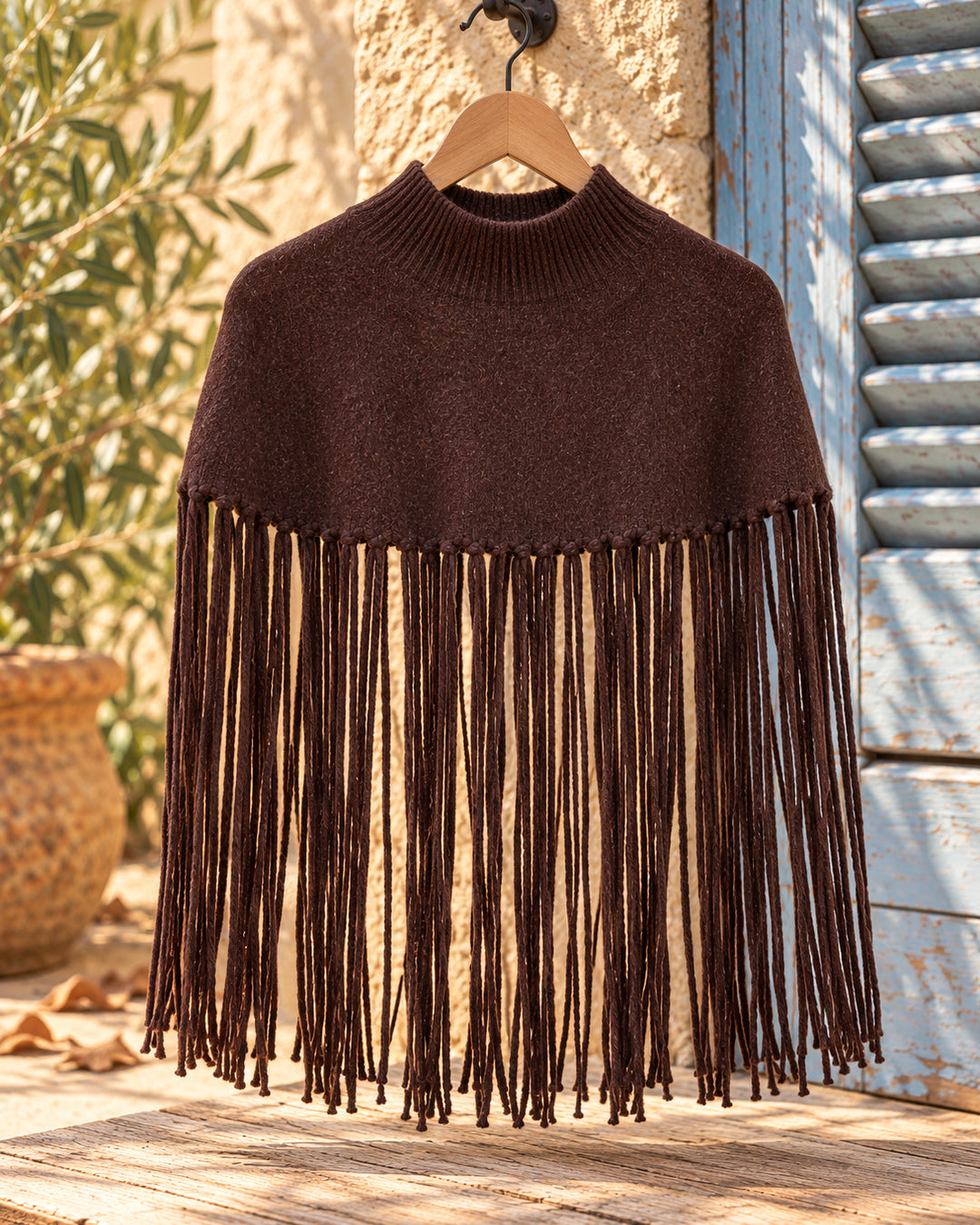 Poncho corto de cuello alto con flecos largos en color chocolate, vista del producto en percha.