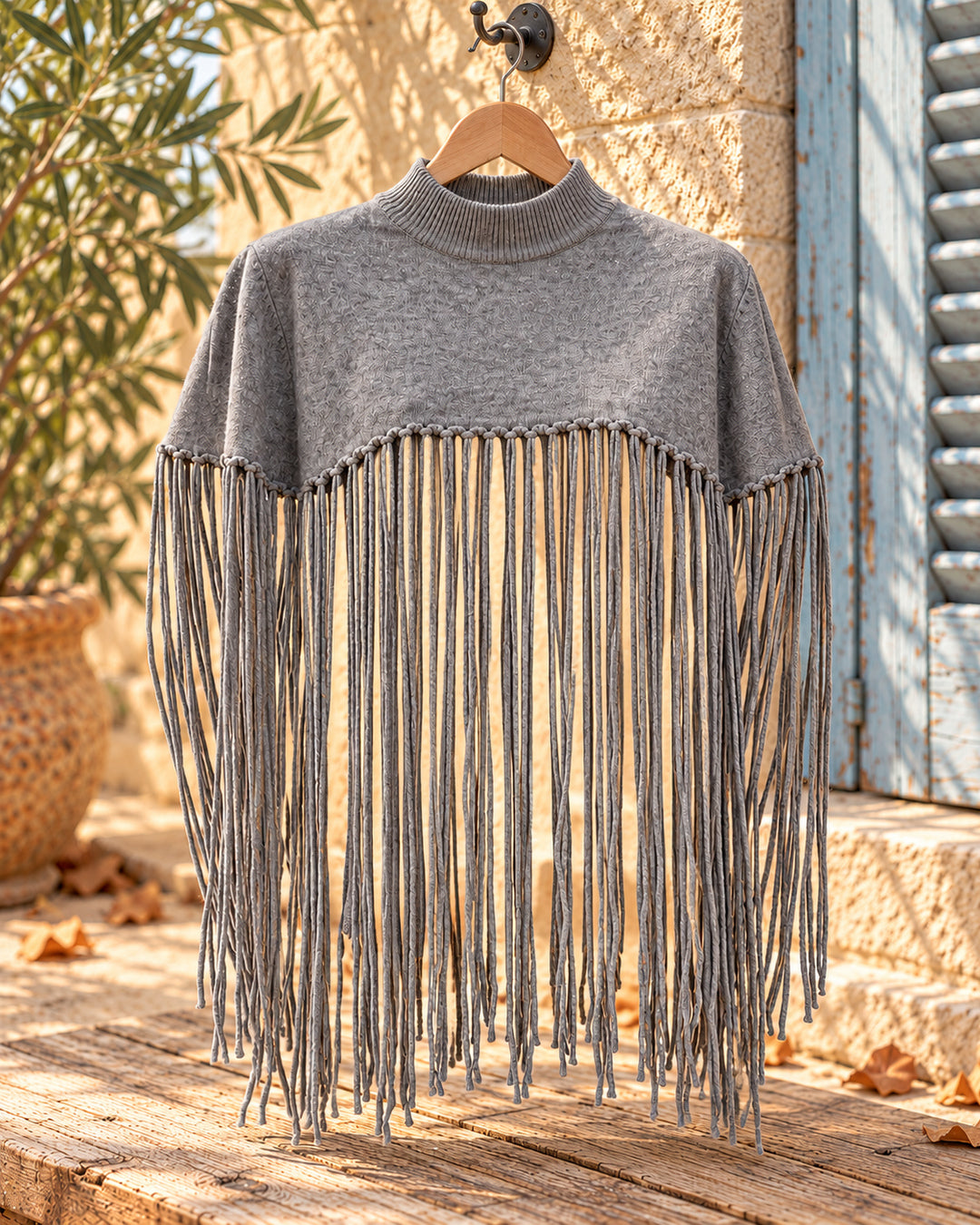 Poncho corto de cuello alto con flecos largos en color gris, vista del producto en percha.