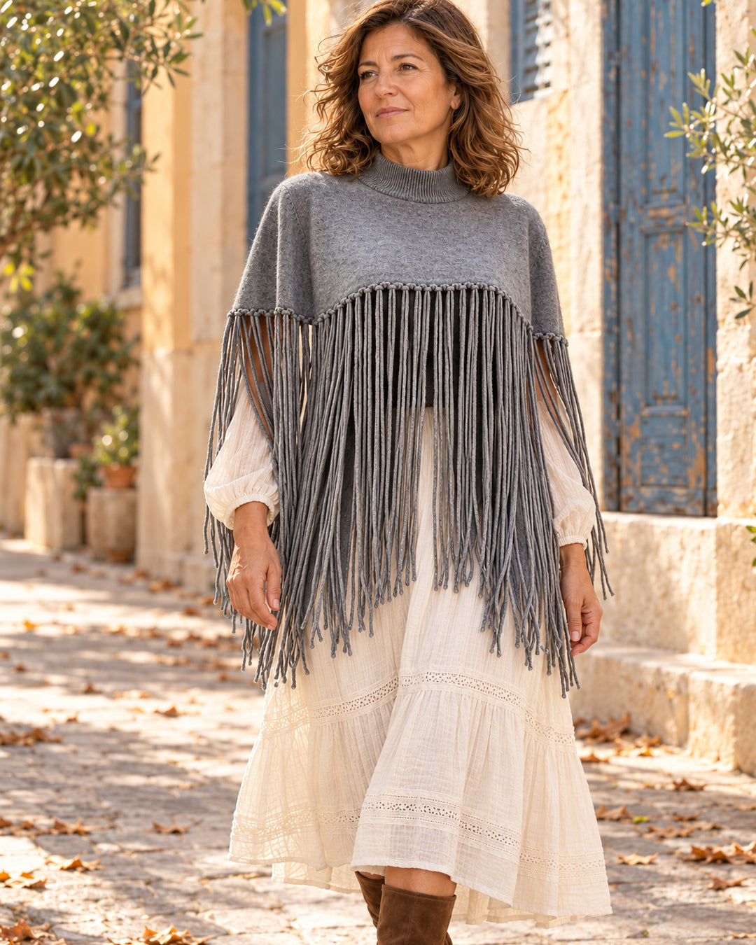 Poncho corto de cuello alto con flecos largos en color gris, llevado sobre vestido marfil.