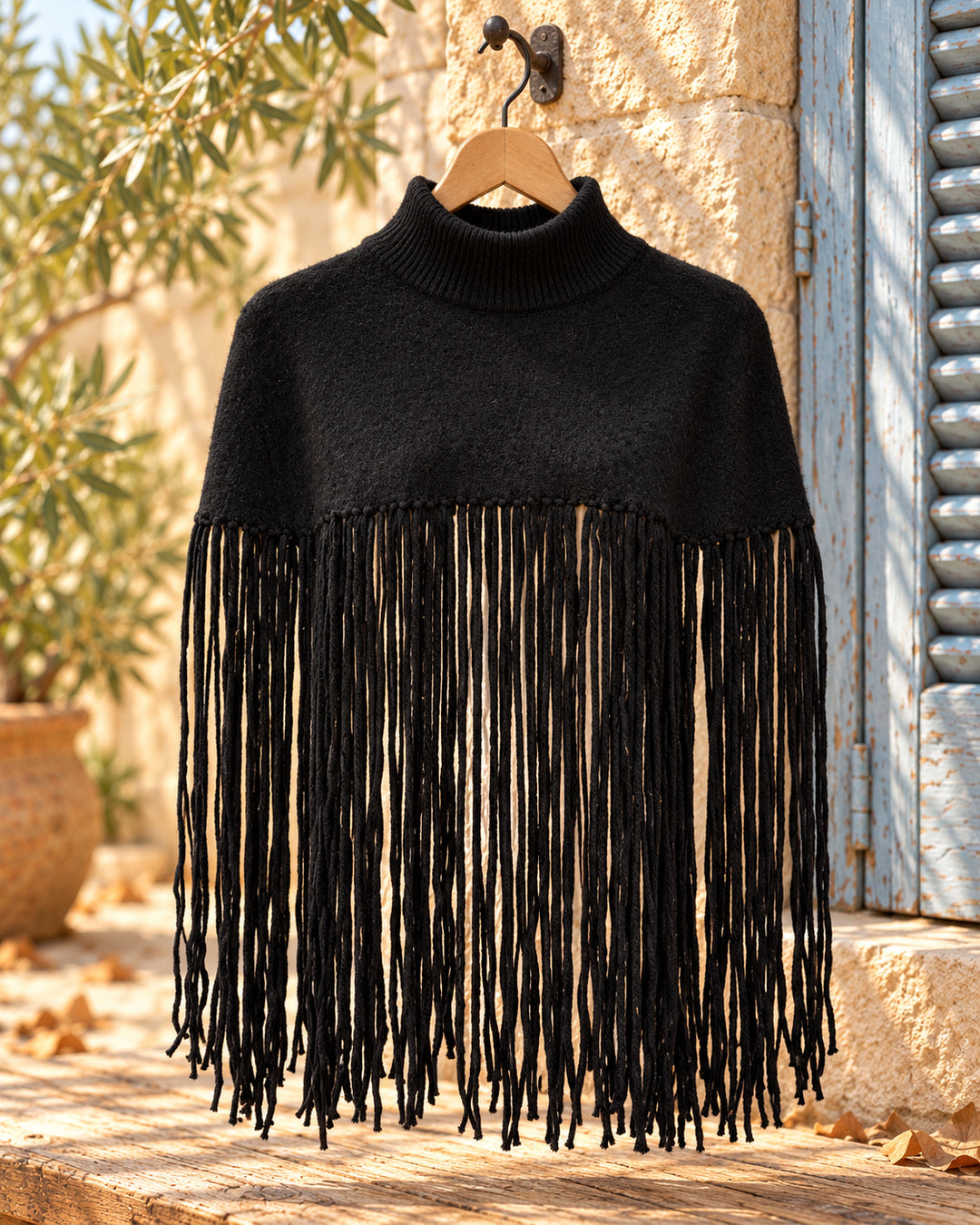 Poncho corto de cuello alto con flecos largos en color negro, vista del producto en percha.