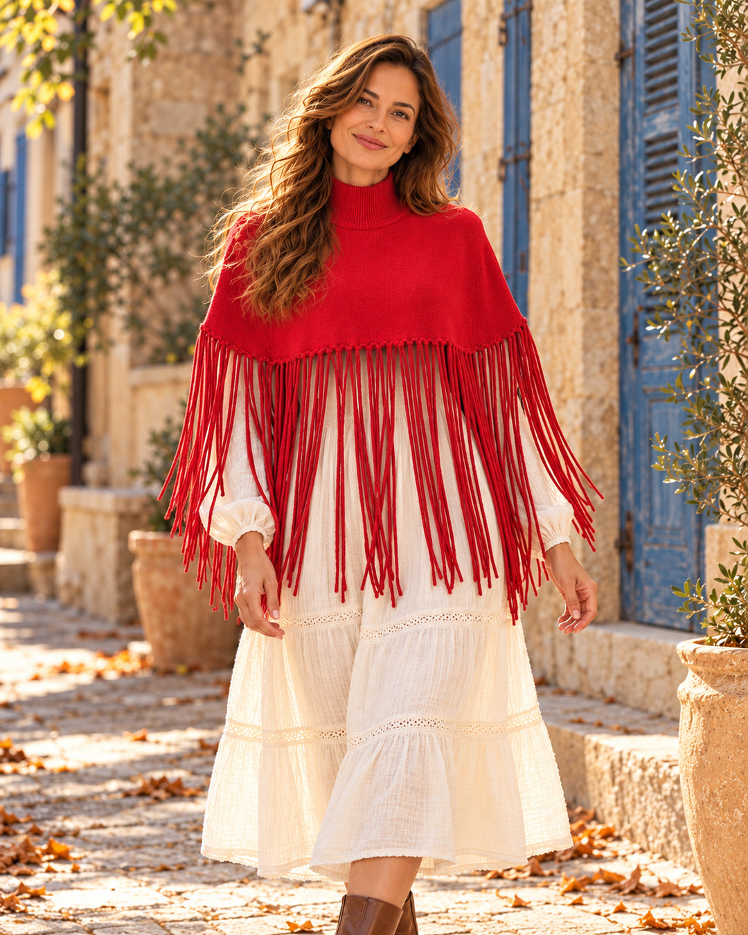 Poncho corto de cuello alto con flecos largos en color rojo, llevado sobre vestido marfil.