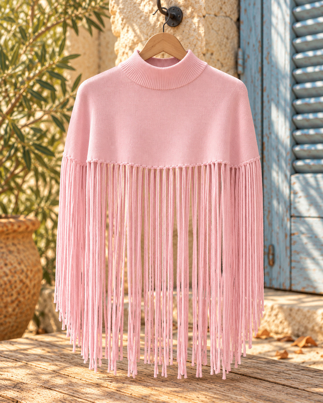 Poncho corto de cuello alto con flecos largos en color rosa, vista del producto en percha.