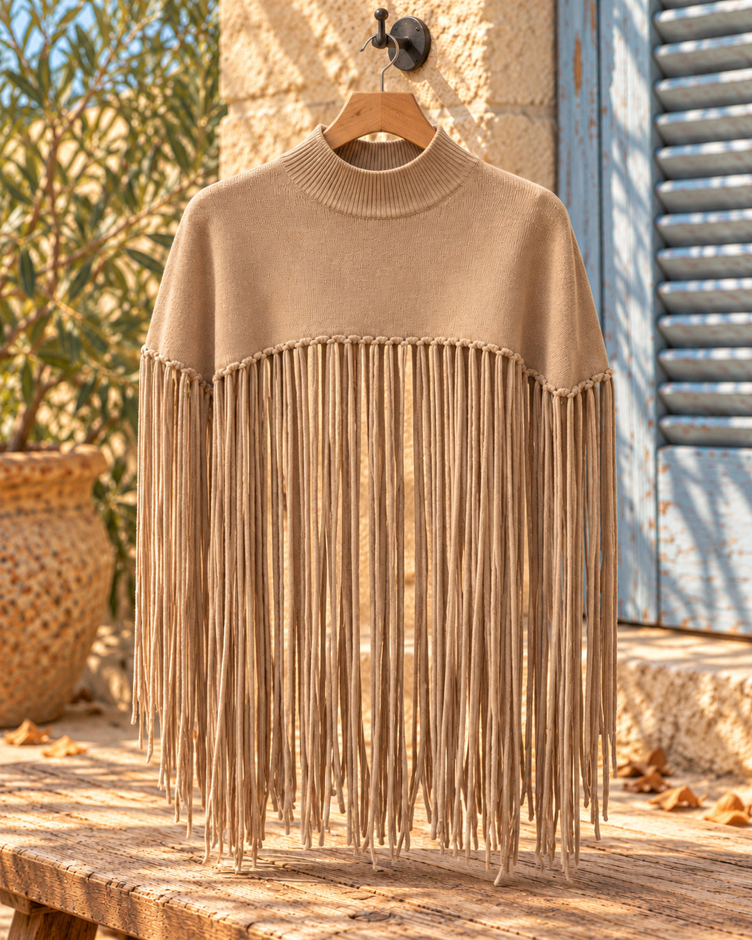 Poncho corto de cuello alto con flecos largos en color topo, vista del producto en percha.