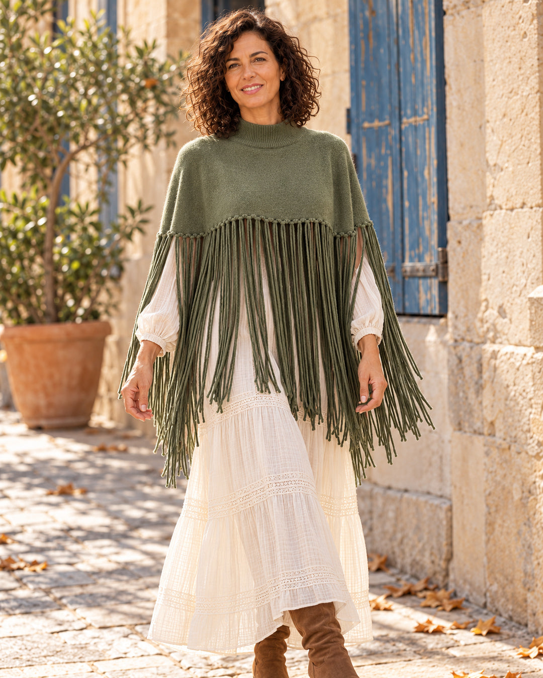Poncho corto de cuello alto con flecos largos en color verde, llevado sobre vestido marfil.